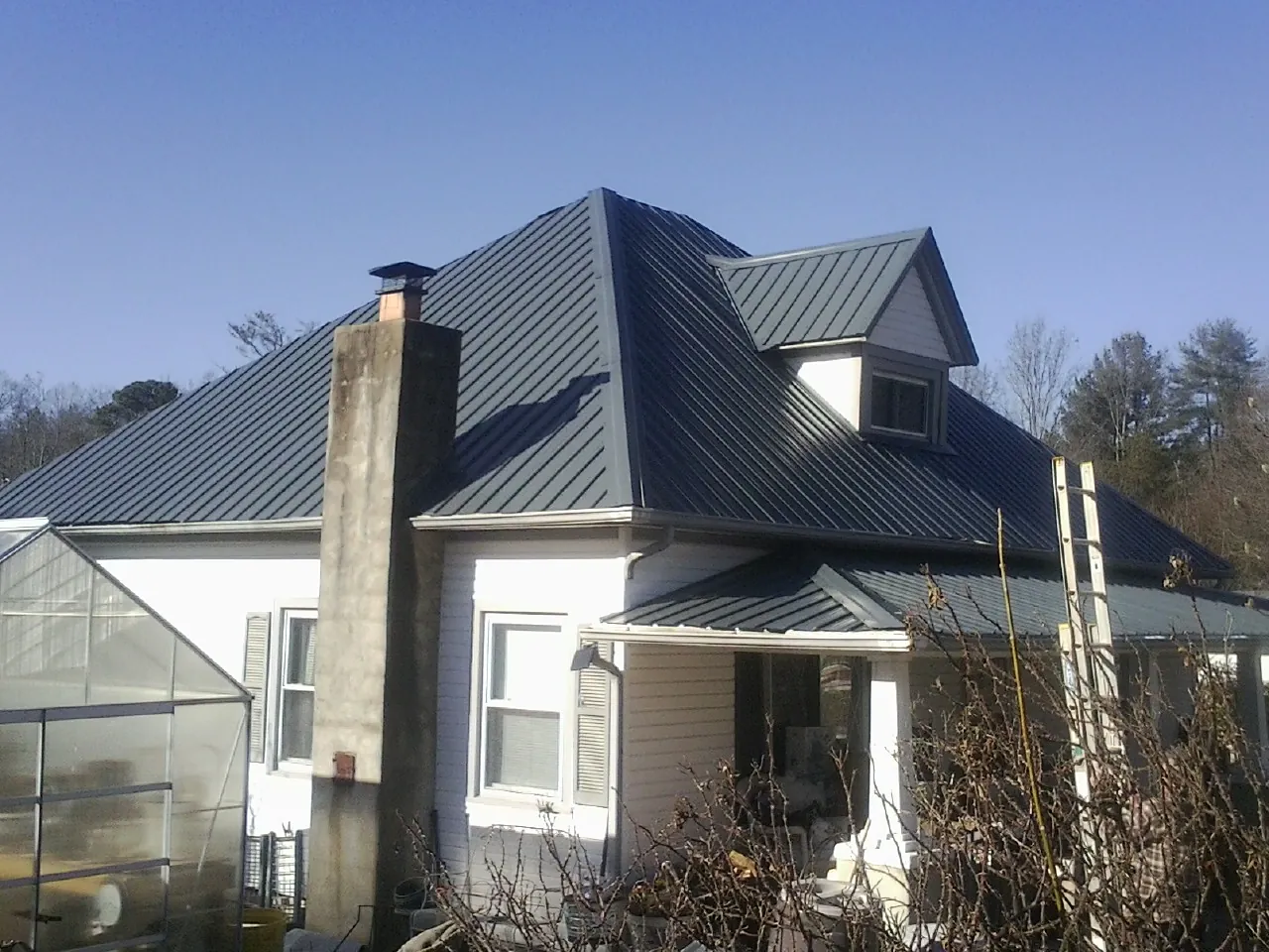 Dark blue standing seam metal roof on a white farmhouse with dormer — Slate & Tile Roof Repair by Roofing Brothers in Cheyney