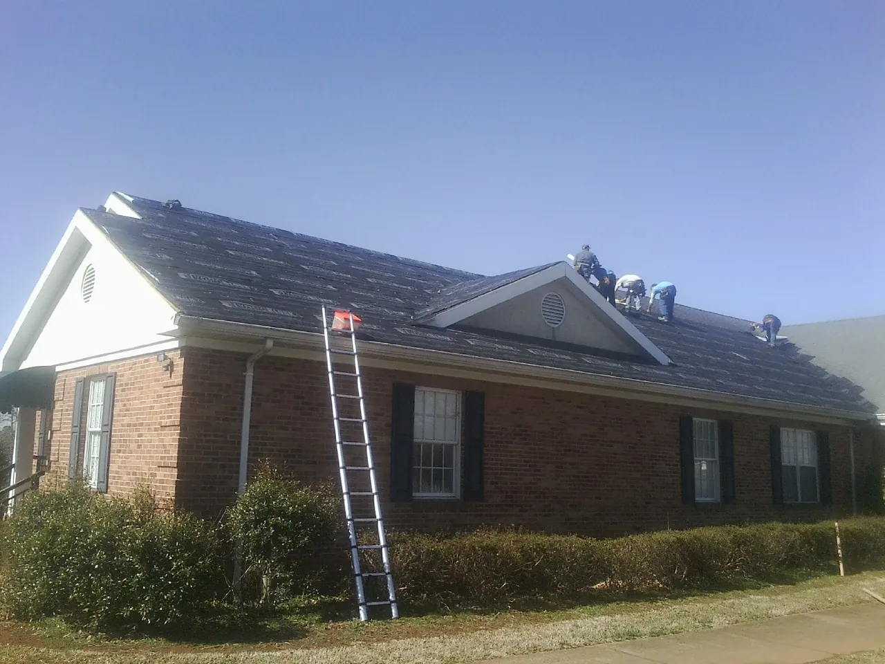 Crew tearing shingles off a brick ranch roof with a ladder set — Metal Roof Repair work by our crew in Cheyney