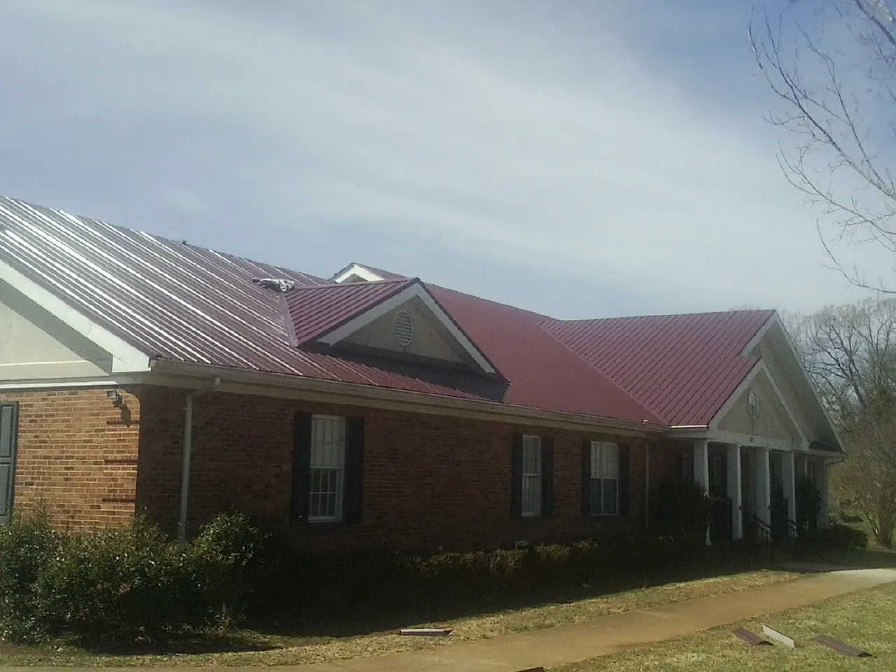 Red metal roof with gabled entries on a long brick building, from a Hail Damage Roof Repair job in Cheyney