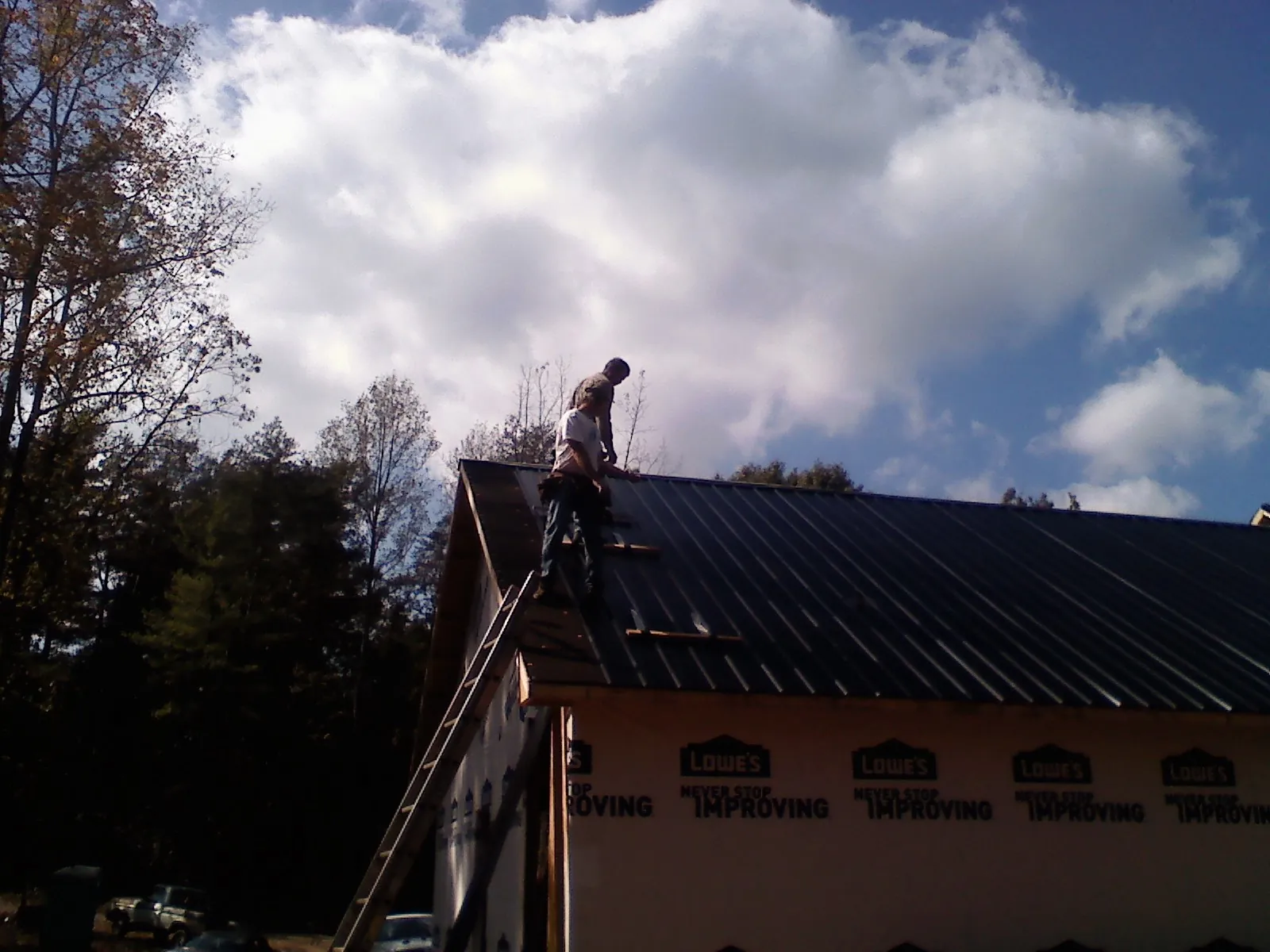 Roofer fastening dark metal panels high against a cloudy sky, from a Roof Inspection job in Cheyney