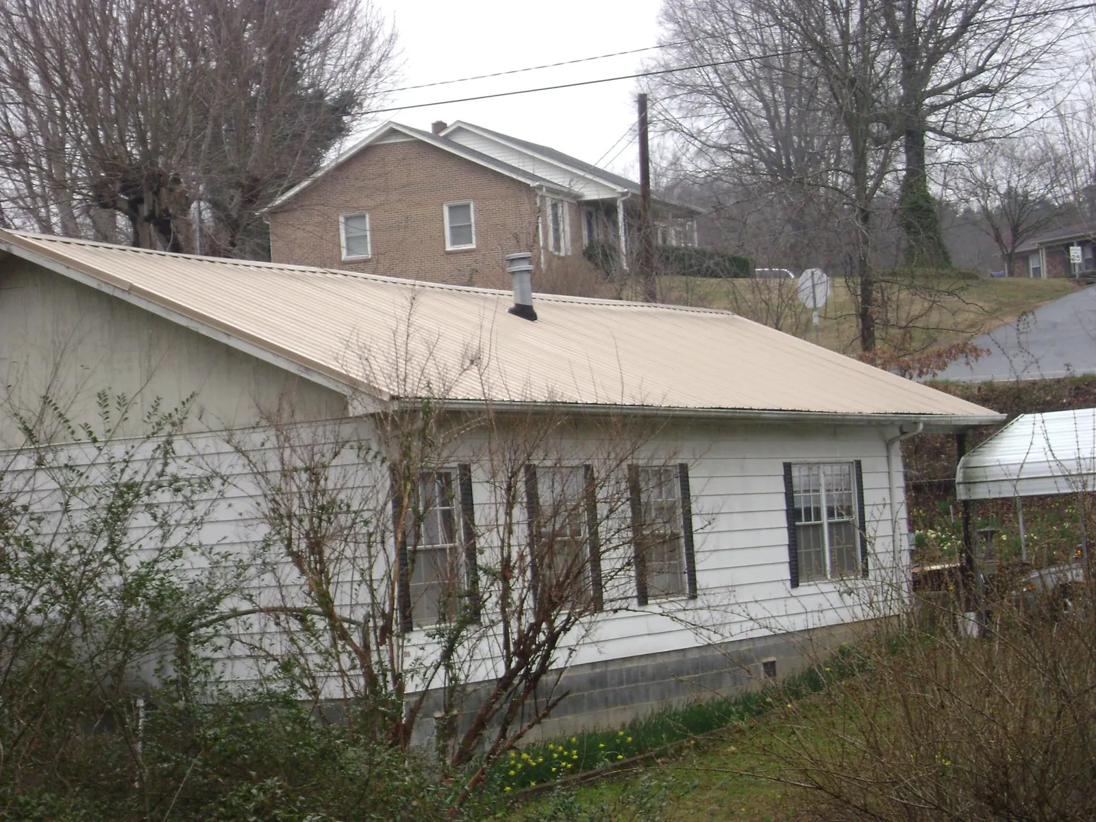Tan metal roof on a white sided house set into a hillside — Commercial Roofing by Roofing Brothers in Cheyney